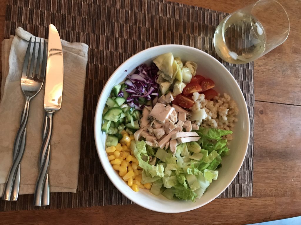 Completed salad bowl with a glass of wine and utensils